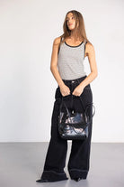 דוגמנית בלבוש קז'ואל: גופיית פסים שחור-לבן, מכנסיים שחורים רחבים ותיק צד עור שחור אופנתי