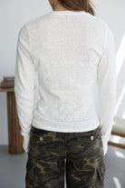 אישה בלבוש אופנתי עם חולצת בד לבנה ארוכה ומכנסי דמוי קאמופלאז' ירוקים, צילום מאחור