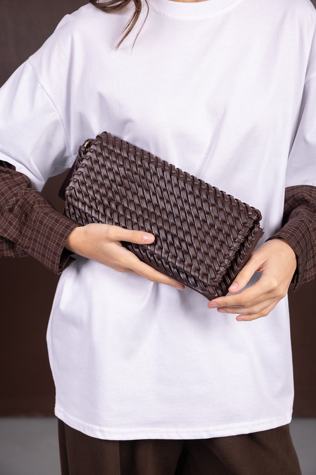 קלאץ' חום קלוע ביד לאישה, אופנת נשים צעירות, שילוב חולצה לבנה ומכנסיים חומים