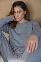 אישה לובשת סט טרנינג אפור, אופנת נשים צעירה, יושבת ומביטה למצלמה