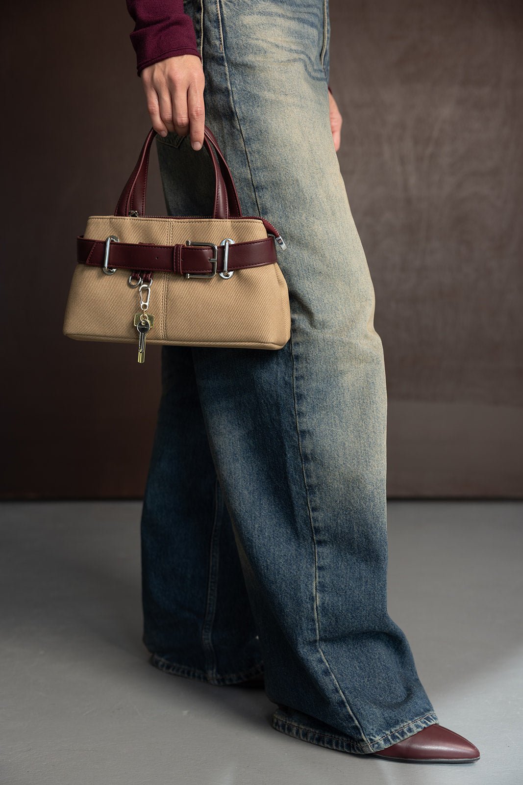 תיק יד אופנתי בז׳ עם רצועות חומות, משולב ג׳ינס רחב ונעל בורדו, אופנה לנשים