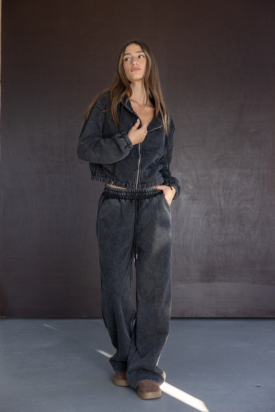 אישה לובשת סט טרנינג שחור אופנתי לנשים עם ז'קט ורוכסן ומכנסיים רחבים