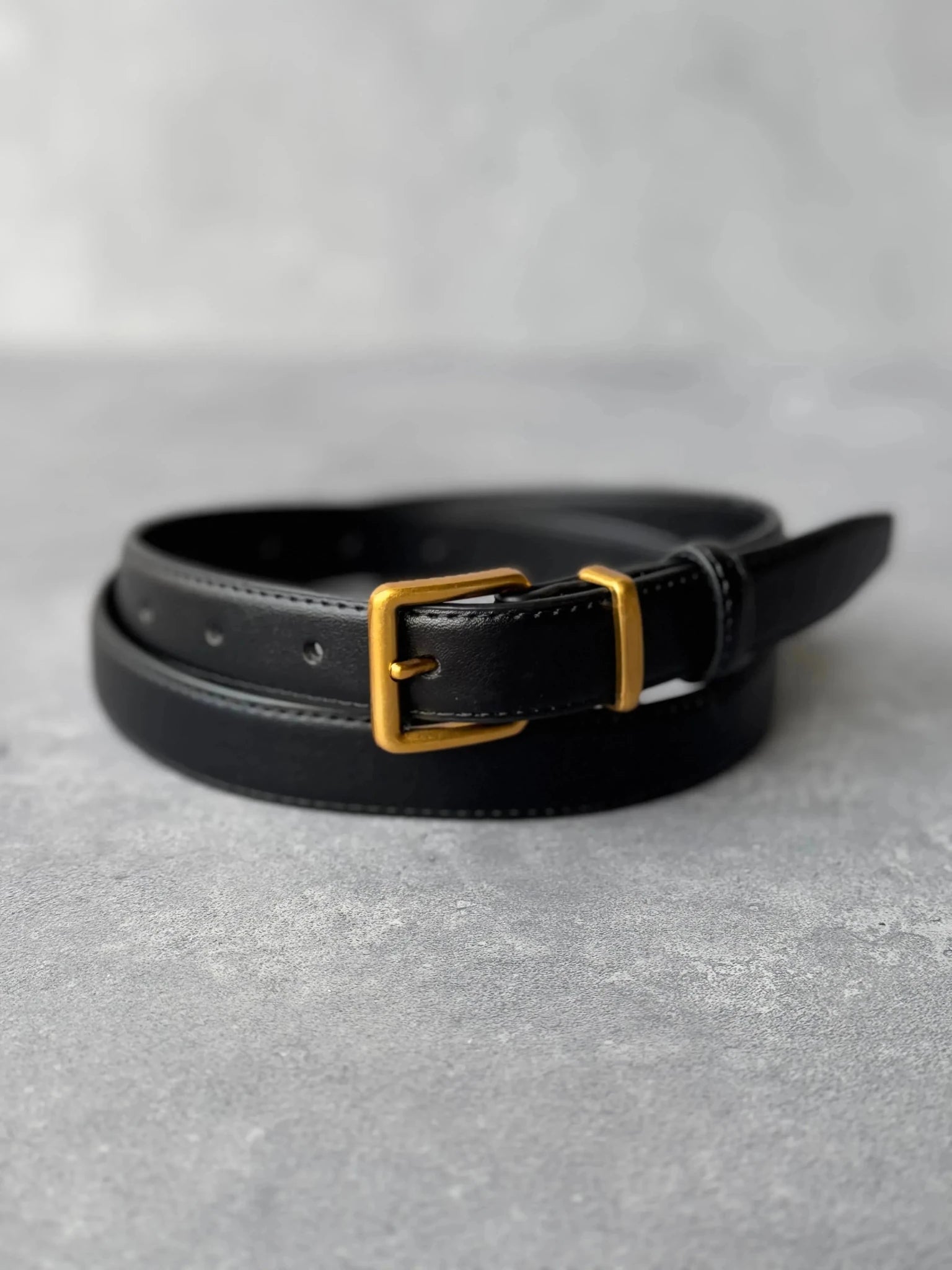 חגורת עור שחורה לאישה עם אבזם מתכת זהב על רקע אפור, אקססורי אופנתי לנשים