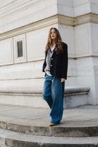 אופנת רחוב לנשים, דגם ג'קט כחול עם כפתורים, סוודר אפור ומכנסי ג'ינס רחבים, רקע עירוני קלאסי