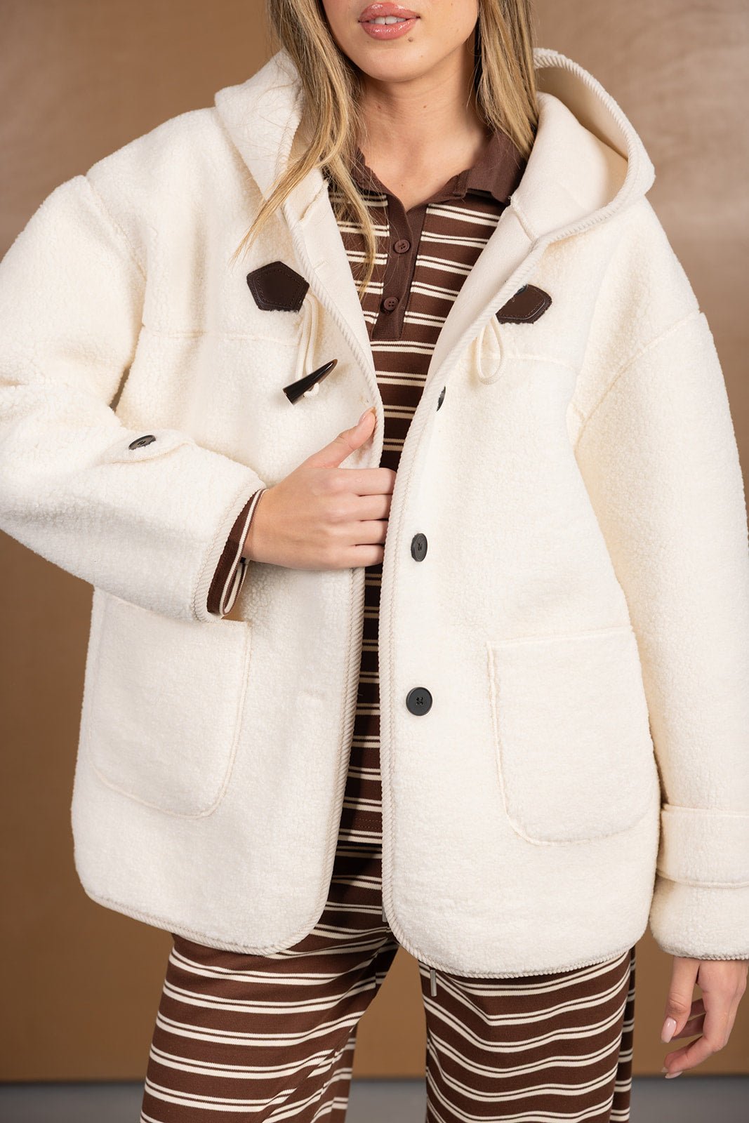 מעיל נשים לבן מבד פרוותי עם כפתורים, בשילוב חולצה ומכנסיים פסים חומים