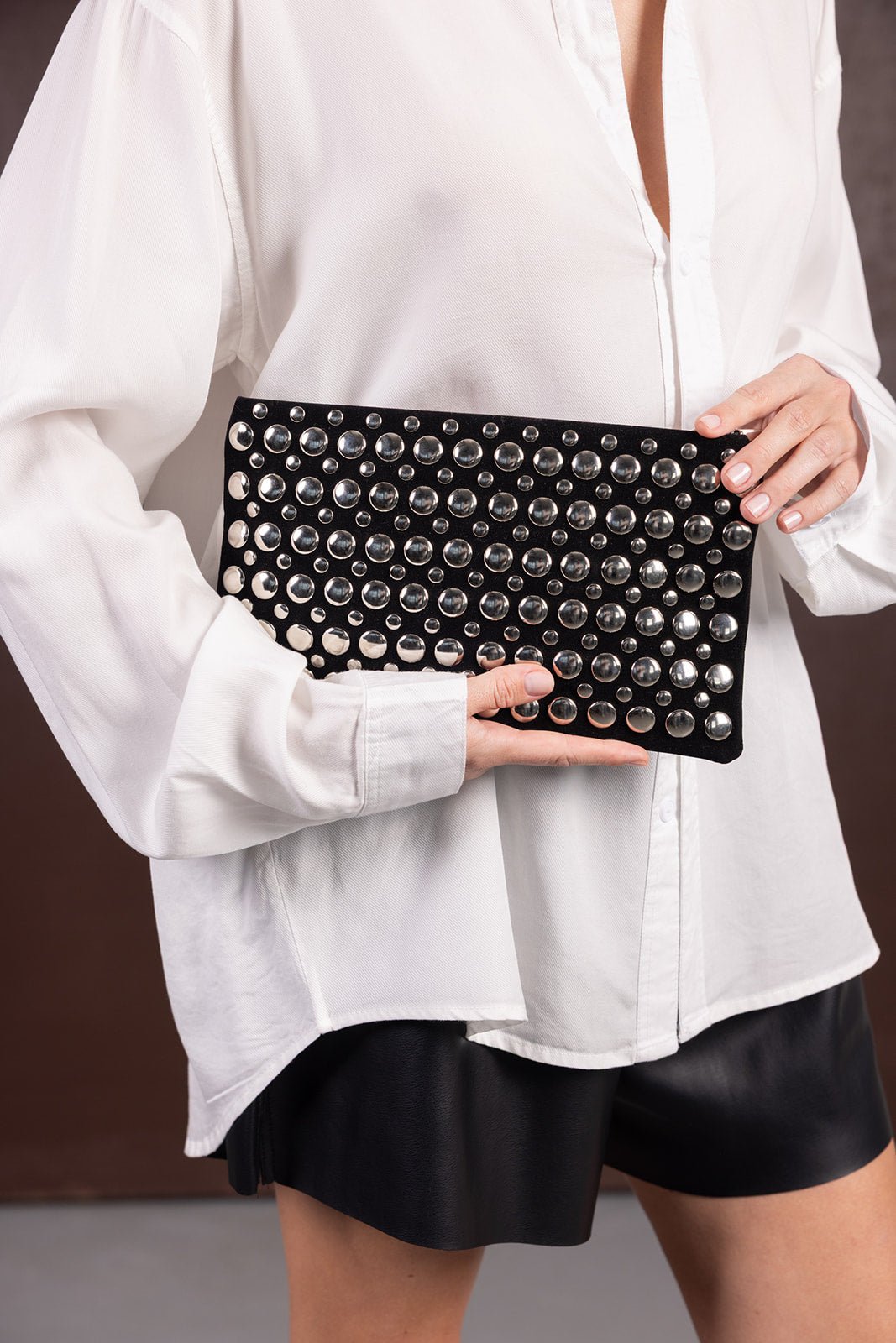 אישה עם חולצה לבנה וחצאית שחורה מחזיקה קלאץ' שחור עם ניטים כסופים, אופנת נשים טרנדית