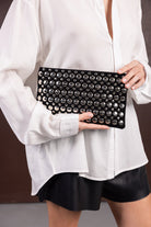 אישה עם חולצה לבנה וחצאית שחורה מחזיקה קלאץ' שחור עם ניטים כסופים, אופנת נשים טרנדית