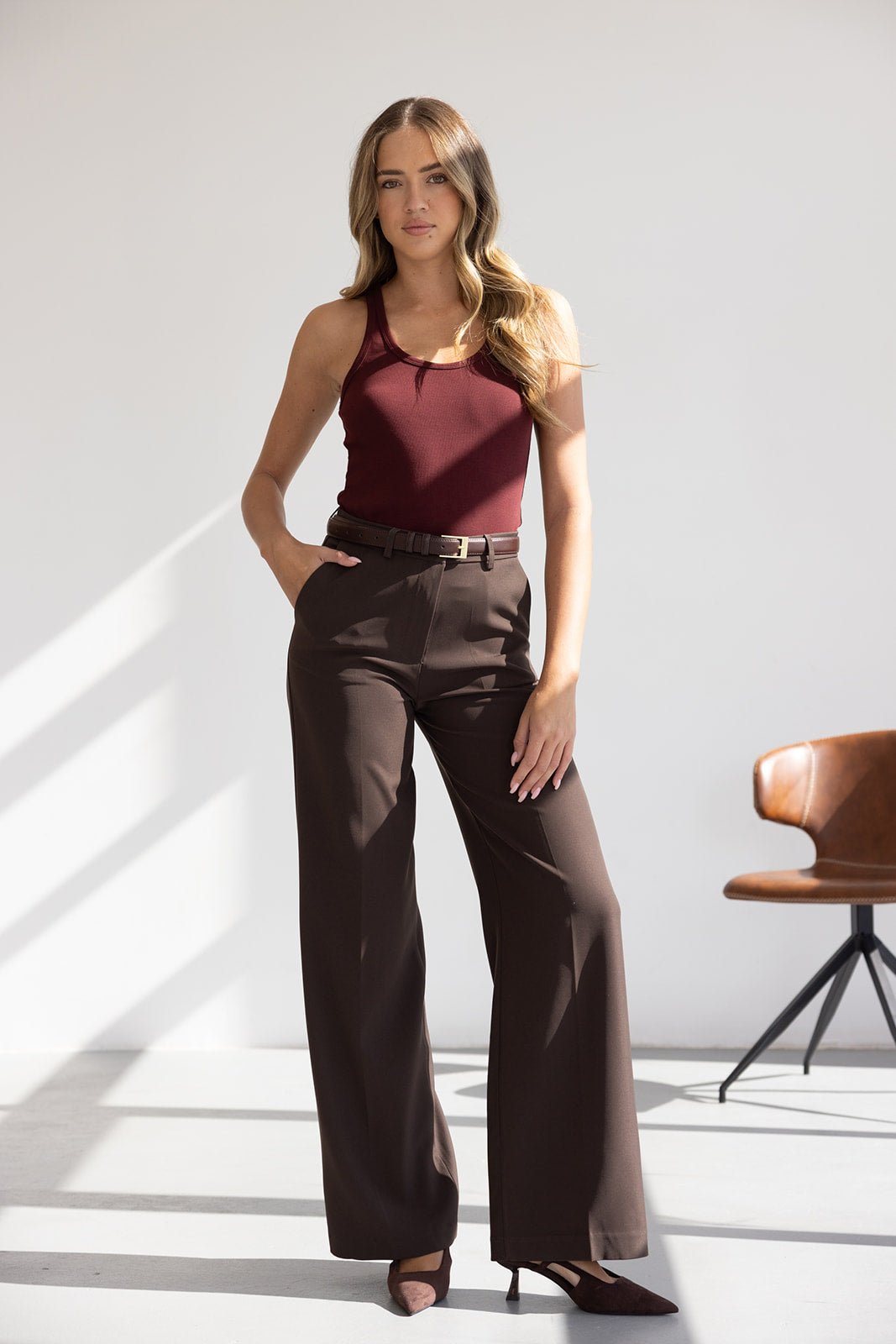 אישה לובשת גופיית בורדו ומכנסיים מחויטים חומים, אופנה קלאסית לנשים, צילומי סטודיו