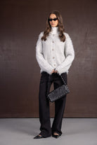 דוגמנית עם סוודר אפור פרוותי, גולף לבן, מכנסיים שחורים, תיק צד שחור ומשקפי שמש אופנתיים