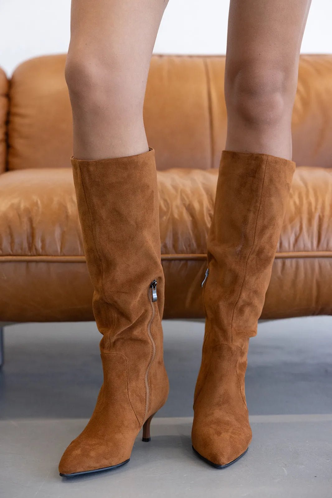 מגפי זמש גבוהים בצבע חום לנשים, עקב דק, מראה אופנתי, על רקע ספה חומה