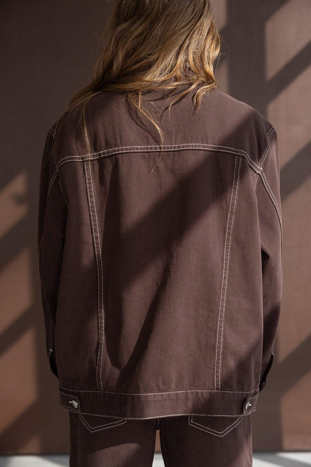 מעיל ג'ינס חום לאישה עם תפרים בולטים, מבט מאחור, אופנת נשים עדכנית