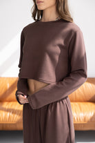 אישה לובשת סט טרנינג חום, חולצת קרופ שרוול ארוך ומכנסיים תואמים, אופנת נשים צעירה