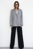 דוגמנית עם משקפי ראייה לובשת בלייזר אפור מחויט ומכנסיים שחורים רחבים, מראה אופנתי לנשים