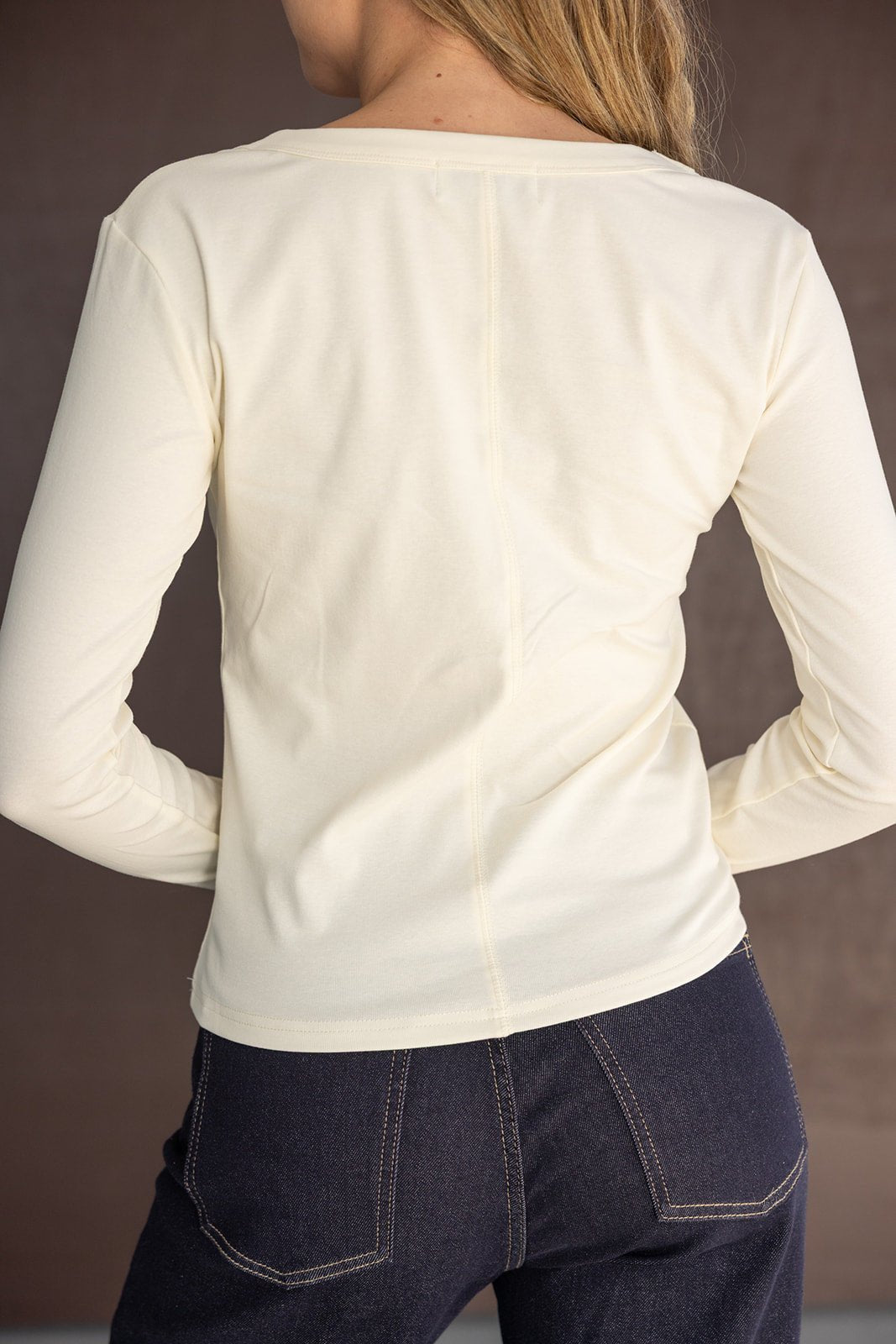 חולצת נשים ארוכה בצבע שמנת עם תפר מרכזי, ג'ינס כהה, מראה אחורי אופנתי