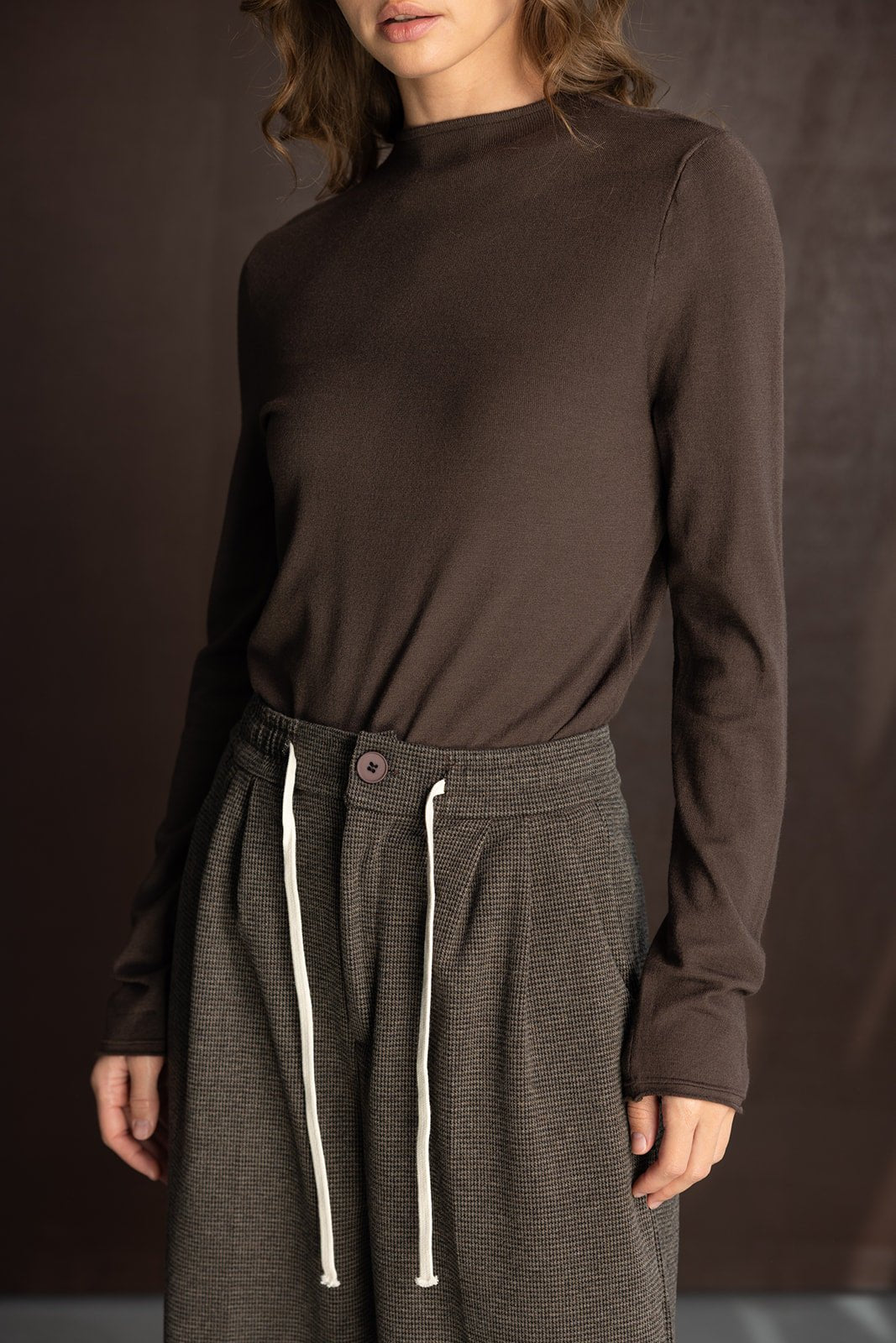 דוגמנית עם חולצה חומה ארוכה ומכנסיים רחבים משובצים עם חוט קשירה, אופנת נשים עדכנית