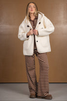 דוגמנית לובשת מעיל פרווה לבן עם מכנסיים חומים מפוספסים, אופנת חורף לנשים