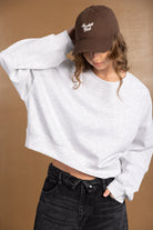 אופנת נשים: דוגמנית עם סווטשירט לבן קצר, ג'ינס שחור וכובע חום עם כיתוב רקום