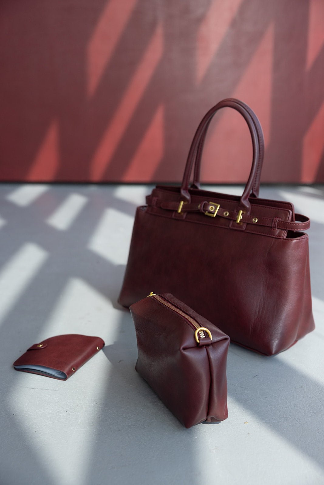 סט תיקי עור לנשים בצבע בורדו, כולל תיק יד, ארנק וקלאץ' אופנתי על רצפת בטון