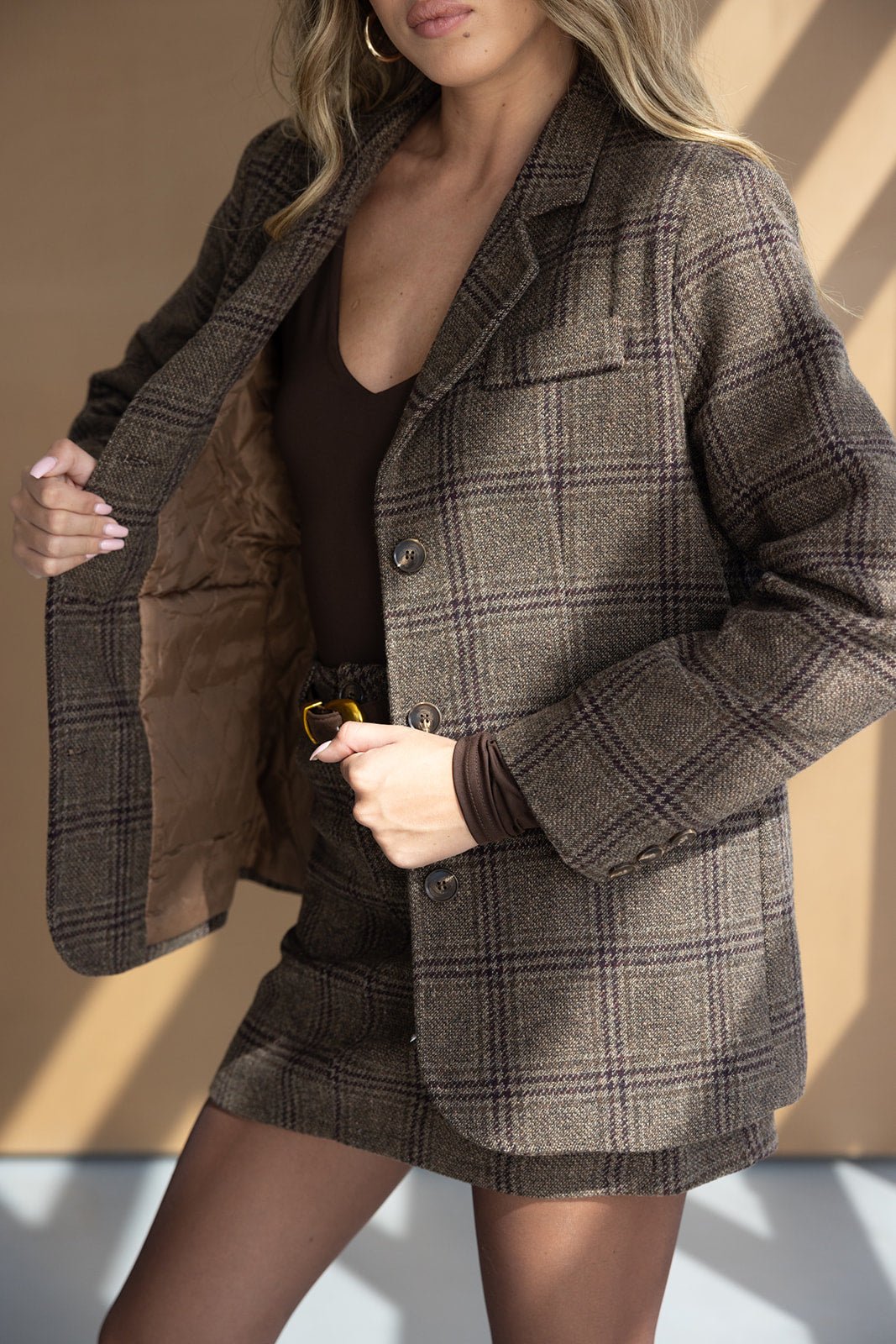 אישה לובשת בלייזר וחצאית משובצים בגווני חום, חולצה חומה ארוכה, אופנה לנשים צעירות