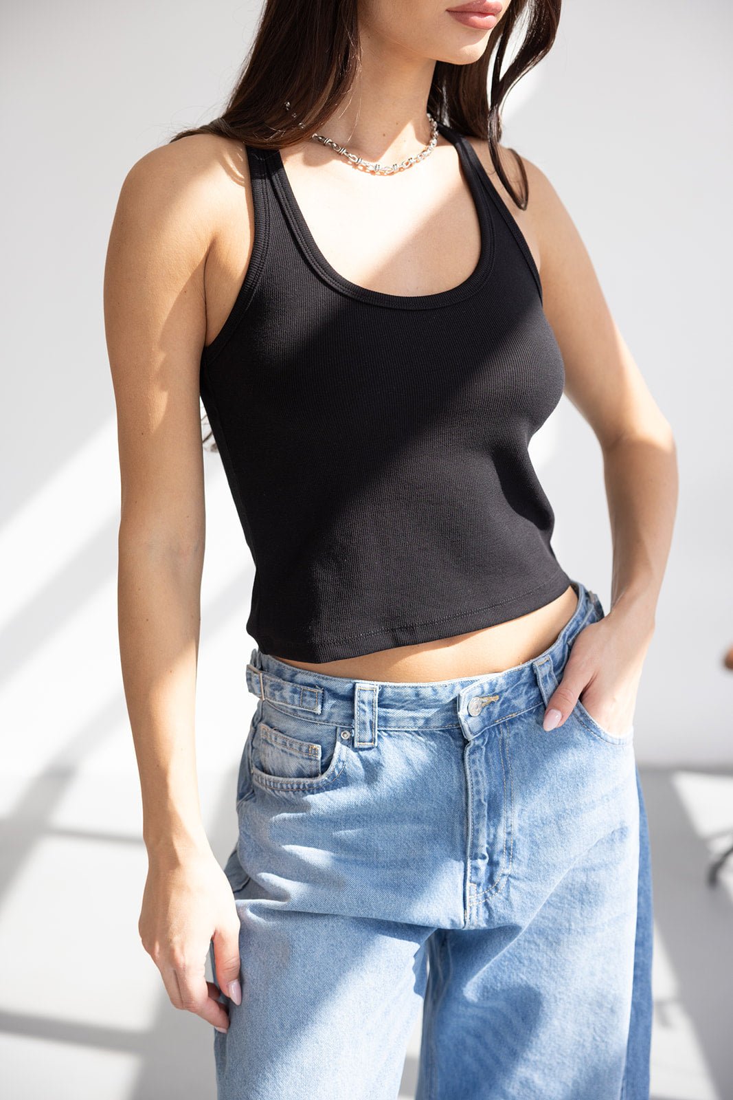 אישה עם גופיית ריב שחורה בגזרת קרופ ומכנסי ג'ינס בגזרה גבוהה, אופנת קיץ לנשים