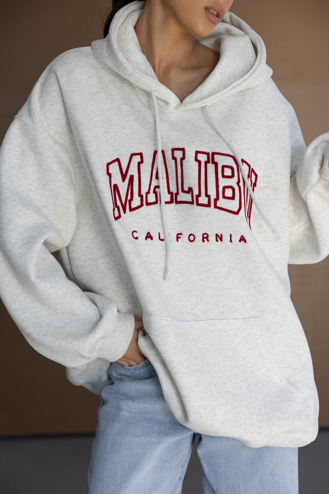 אישה לובשת קפוצ'ון אפור עם כיתוב MALIBU CALIFORNIA ואופנת ג'ינס לנשים צעירות