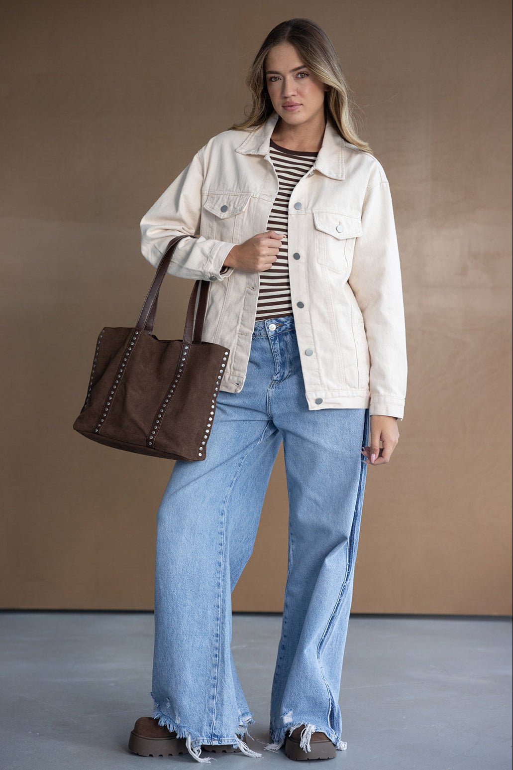 אישה עם ג'קט בז', חולצה מפוספסת, ג'ינס רחב ותיק חום, טרנד אופנה לנשים צעירות