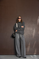 אישה עם סווטשירט אפור, מכנסיים רחבים אפורים, תיק שחור ומשקפי שמש אופנתיות, לוק חורפי ונשי