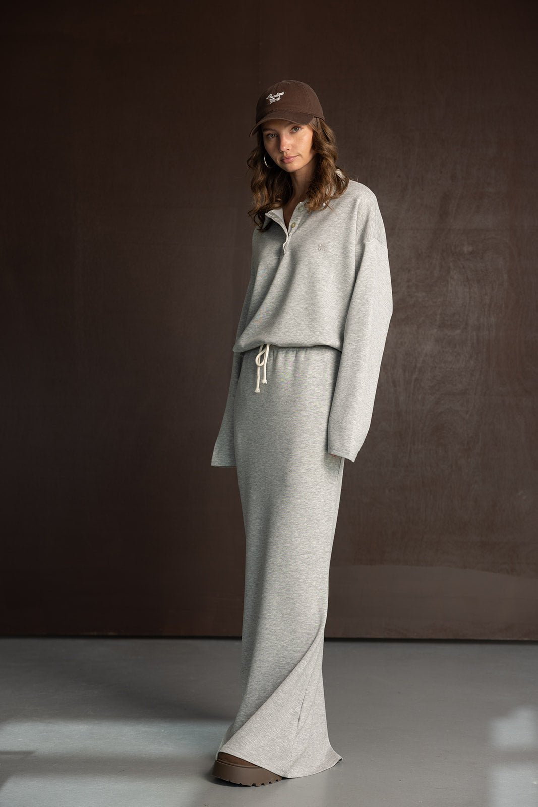 דוגמנית עם שמלת טרנינג אפורה וכובע חום, אופנה נוחה לנשים, רקע כהה