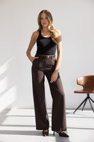 אישה לובשת גופייה שחורה ומכנסיים חומים מחויטים, אופנת נשים צעירה, סטודיו מואר