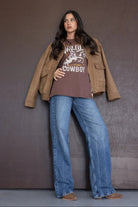 אישה עם חולצת טישירט חומה בהדפס קאובוי, ז'קט חום ומכנסי ג'ינס רחבים, לוק קז'ואל טרנדי לנשים