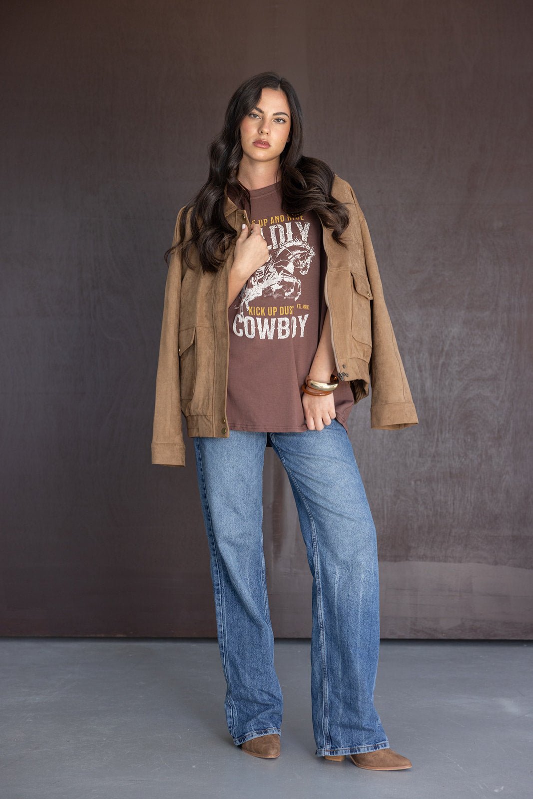 אישה לובשת מעיל חום, חולצת טי קאובוי חומה וג'ינס רחב, לוק אופנתי לנשים צעירות