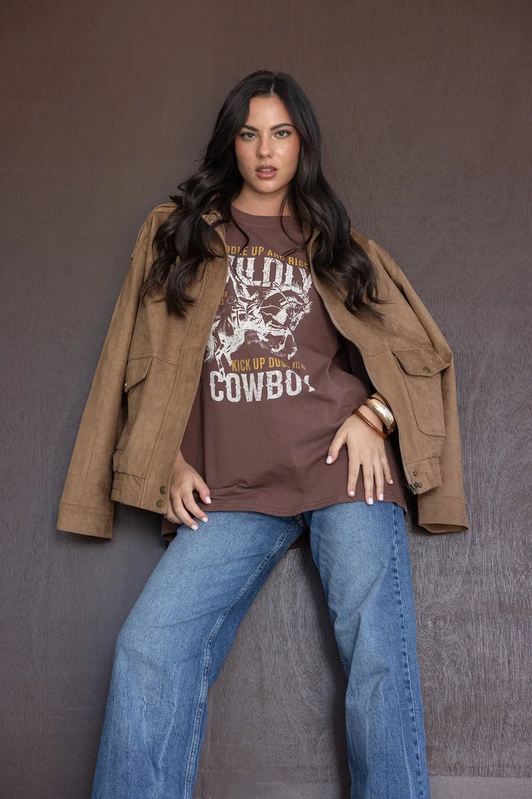 דוגמנית לובשת חולצה חומה עם הדפס קאוובוי, ג'קט בז' ומכנסי ג'ינס רחבים, אופנת נשים צעירה